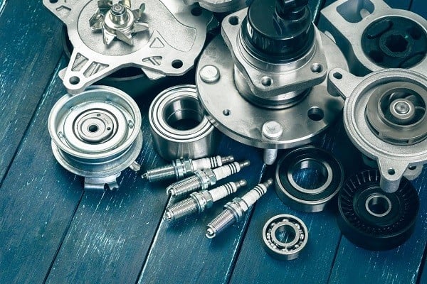 A collection of various car engine parts including bearings, spark plugs, and pulleys, arranged on a blue wooden surface.